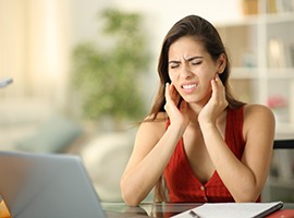 Woman sitting at computer, suffering from TMD symptoms